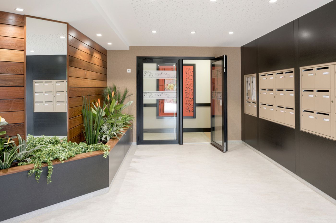 Les 4 Saisons à Anglet : hall d’entrée avec boîtes aux lettres, habillage bois et jardinière.
