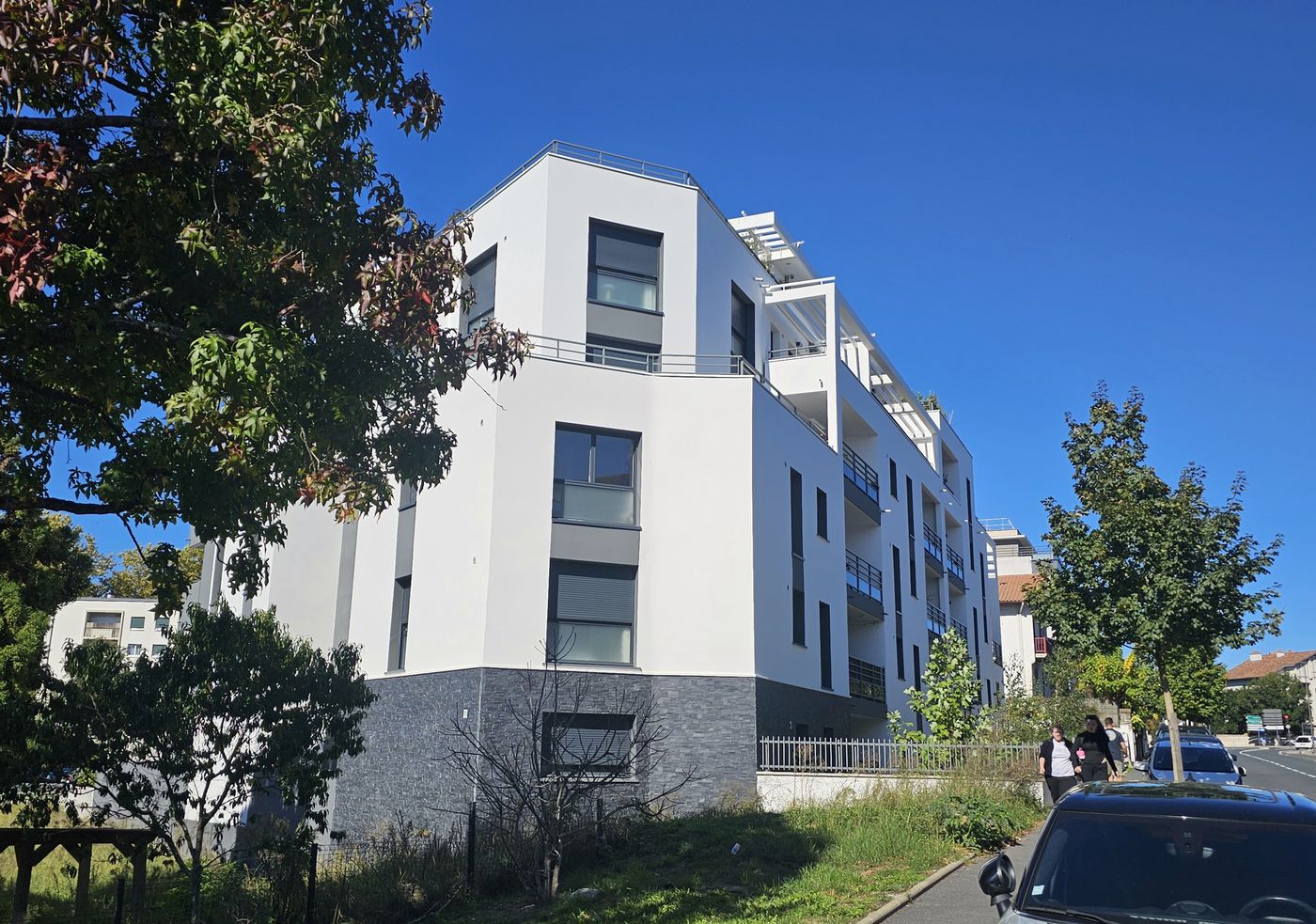 Akoya à Bayonne : façade blanche sur socle de pierre anthracite, terrasses en retrait aux derniers niveaux.