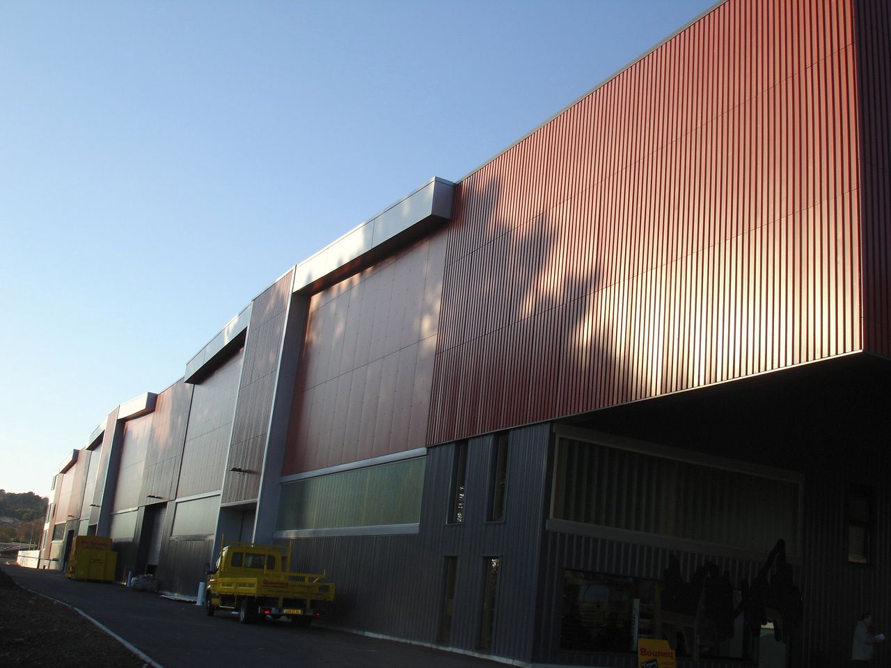 Établissements Bouney à Anglet : façade de l’entrepôt en bardage bois rouge et métal.
