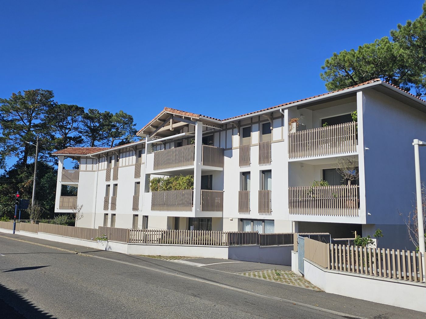 Esprit Océan à Capbreton : façade sur rue, loggias en bois et toiture en tuiles, pins maritimes en fond.