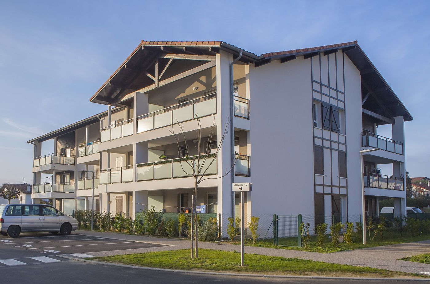 Ibarola à Saint-Pée-sur-Nivelle : immeuble à charpente apparente et balcons, au bord de la voie.