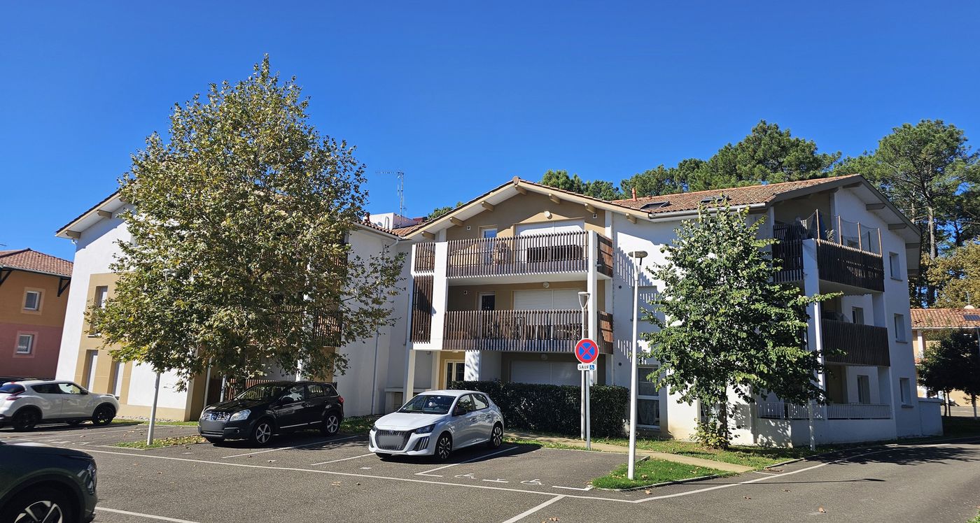 Loustaou à Labenne : bâtiment de logements à balcons en bois, entouré d’arbres.