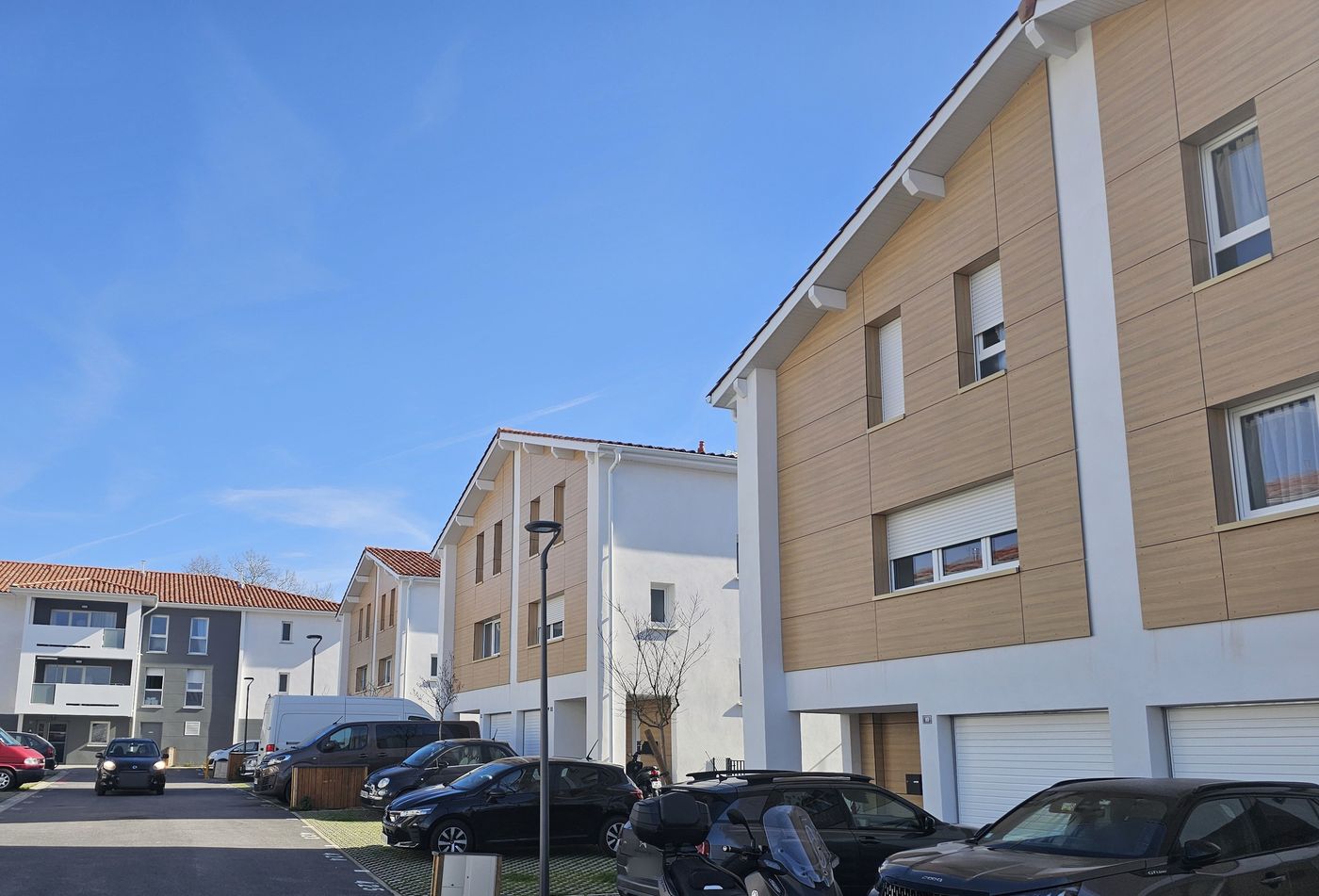 Zura à Bayonne : façades à bardage bois clair le long de la voie, garages en rez-de-chaussée.