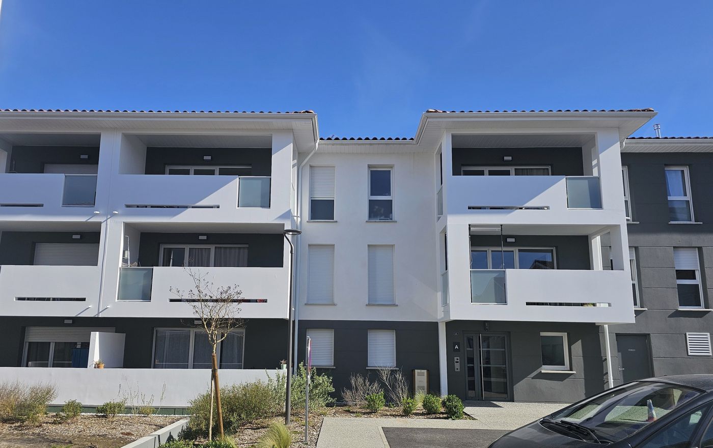 Zura à Bayonne : façade de logements sur socle sombre, cheminement planté.